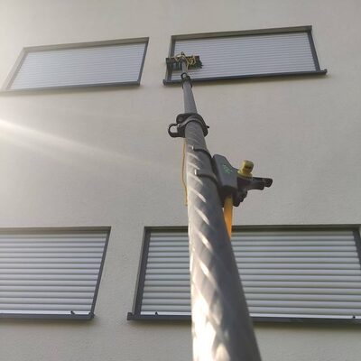 Teleskopstange mit Wasserbürste an den Fenstern eines Obergeschosses