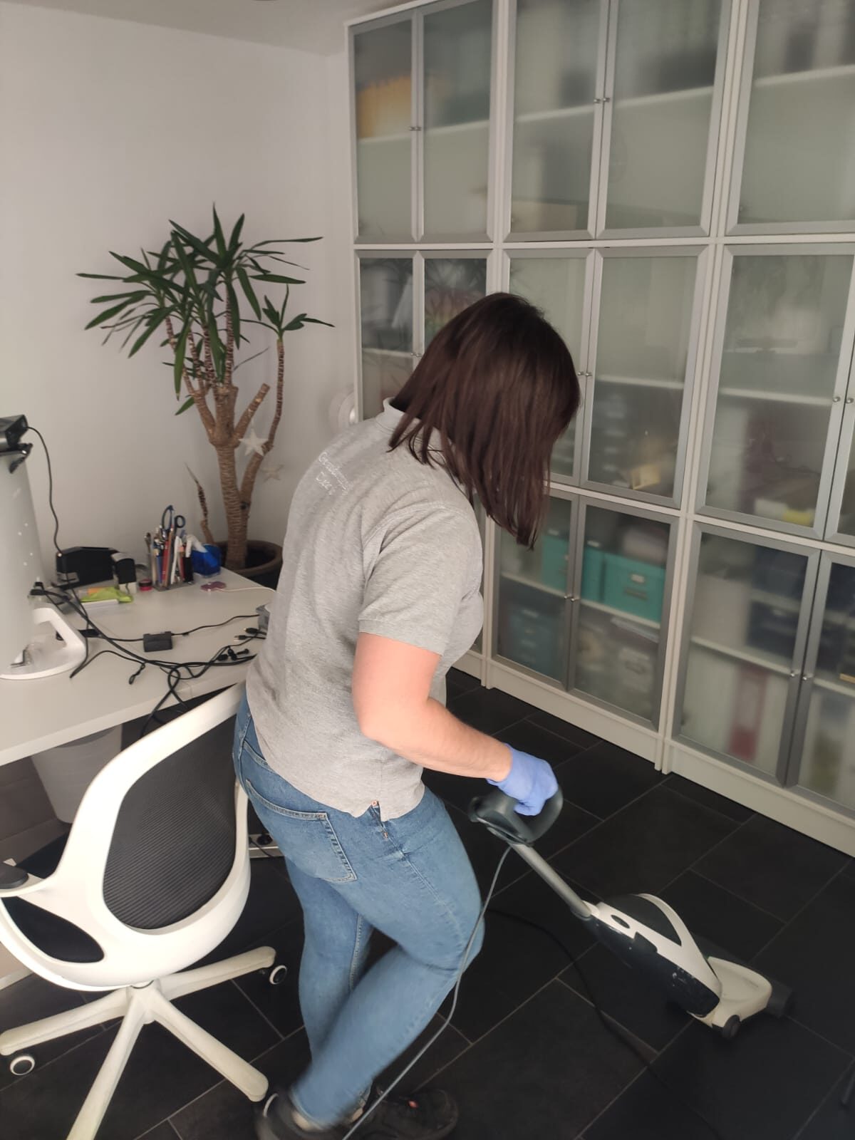 Mitarbeiterin der Clean Lady saugt den Boden in einem Büro mit Schreibtisch und Aktenschrank