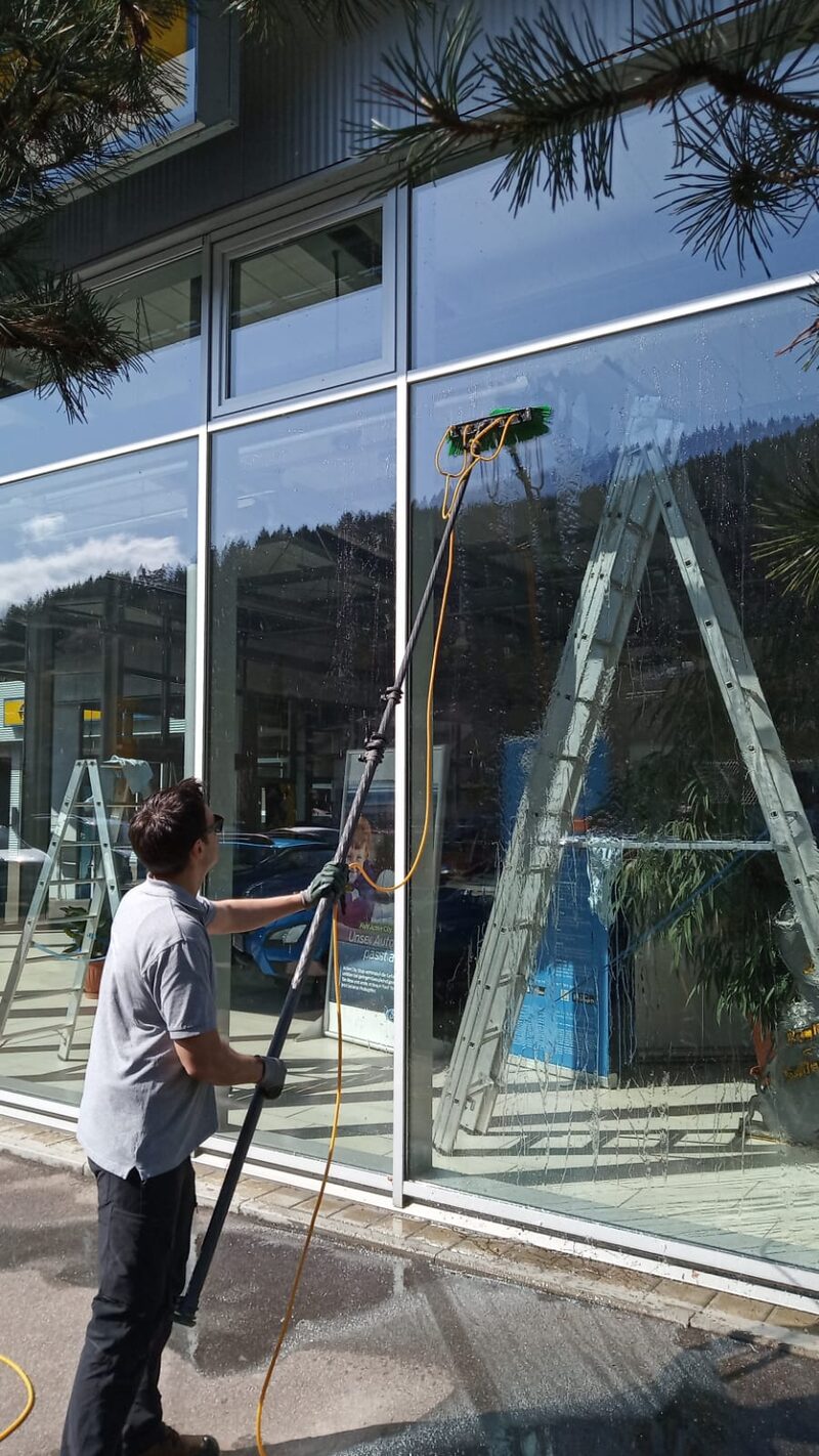 Glasfront eines Autohauses wird mit Teleskopstange und Wasserbürste gereinigt